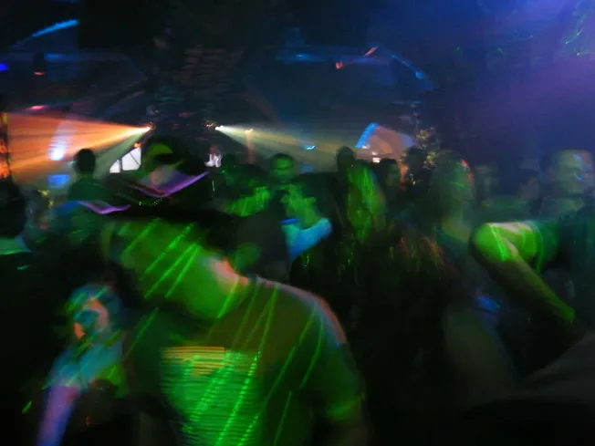 A lively nightclub scene with people dancing under colorful laser lights, creating an energetic and vibrant atmosphere for mu