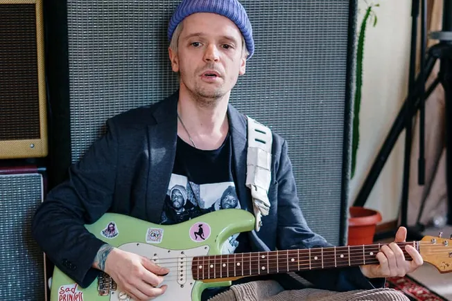 Viral musician playing an electric guitar in a music studio, face focused on performing, surrounded by amplifier speakers and