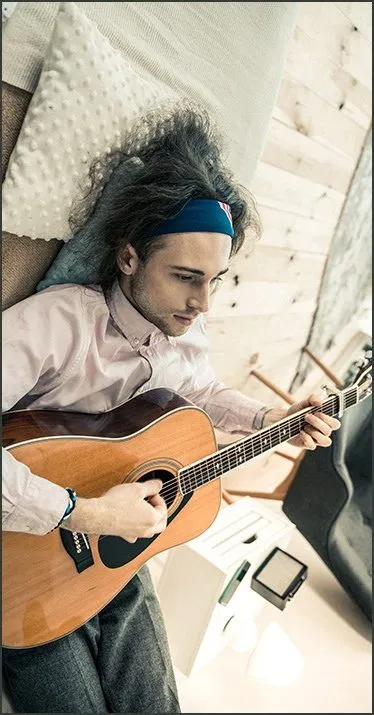 Relaxing woman playing acoustic guitar at home, cozy music session, living room with wooden wall, casual and creative music e