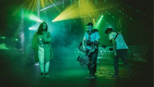 Stylish woman and camera crew preparing for a music event with vibrant stage lighting in a nightclub or concert venue.