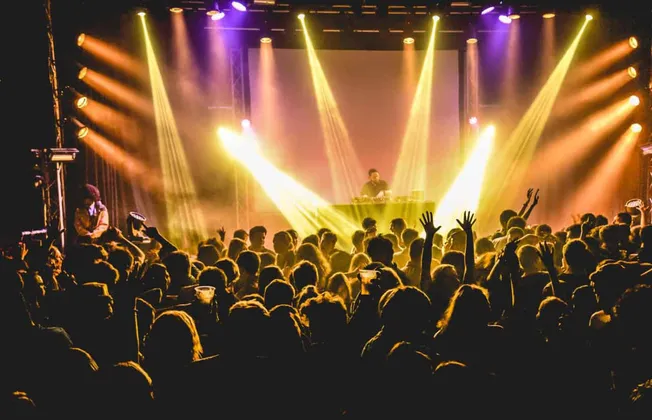 Bright concert scene with DJ and live audience enjoying music, colorful stage lighting, energetic atmosphere, and crowd danci