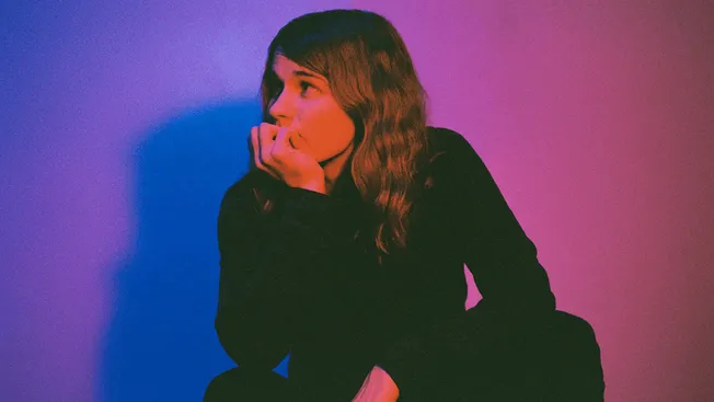 Woman in black long sleeve shirt sitting on floor with colorful lighting, music industry concept.