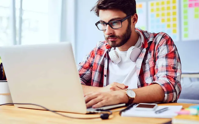 Young man working on laptop with headphones, digital marketing, music industry, or remote work theme.