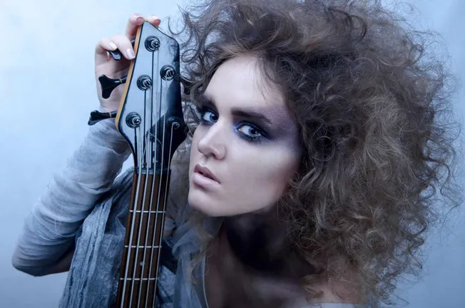 Vibrant image of a woman with curly hair holding a guitar headstock, showcasing modern music aesthetics and artistic expressi