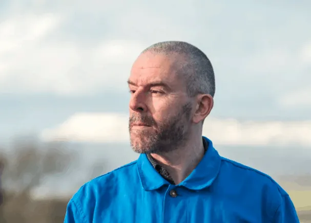 Professional man outdoors wearing a blue jacket, contemplating or observing in a natural setting, representing insights into
