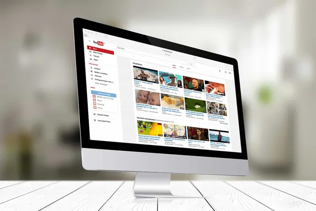 Youtube video platform interface on an iMac monitor, displaying trending and recommended videos, digital content, online vide