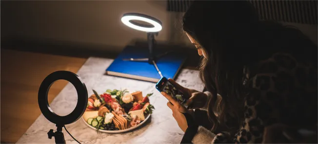 High-quality food photography setup with ring light, woman taking a photo of a charcuterie board, food styling for social med