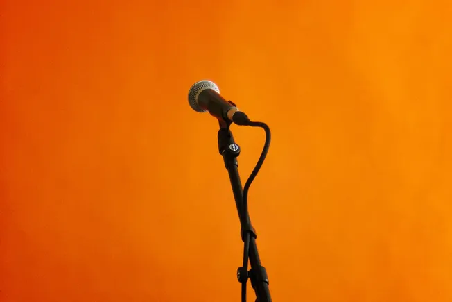 Microphone on a black stand against an orange background, ready for a speech or performance, representing live music, public
