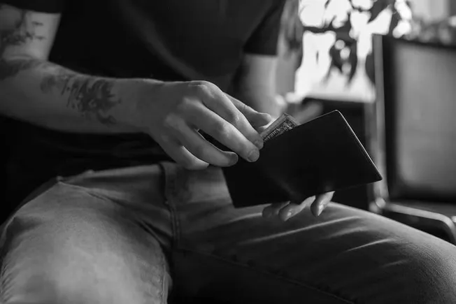 Wallet with cash in hand, person sitting on chair, black and white photo, casual clothing, financial transaction, personal fi