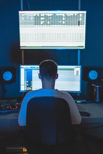 A music producer working in a professional studio with multiple audio monitors and mixing software on a large screen.