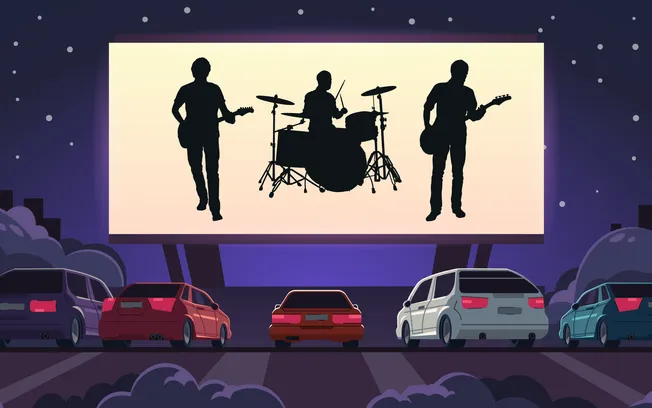 Silhouettes of a band playing on a large outdoor movie screen at night with cars parked in front, creating a lively outdoor c