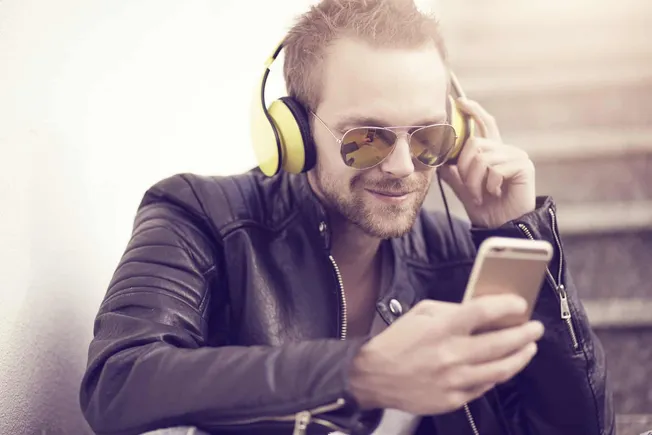 Headphones, sunglasses, and a smartphone—young man enjoying music and digital entertainment outdoors, representing modern mus