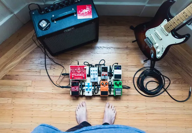 Brightly colored guitar effect pedals connected on a pedalboard, electric guitar, amplifier, and cables on a wooden floor, cr