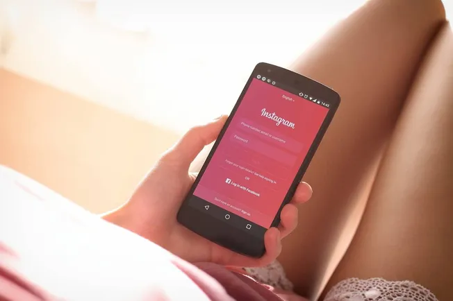Mobile phone displaying Instagram login screen being held in a person's hand on a bed.