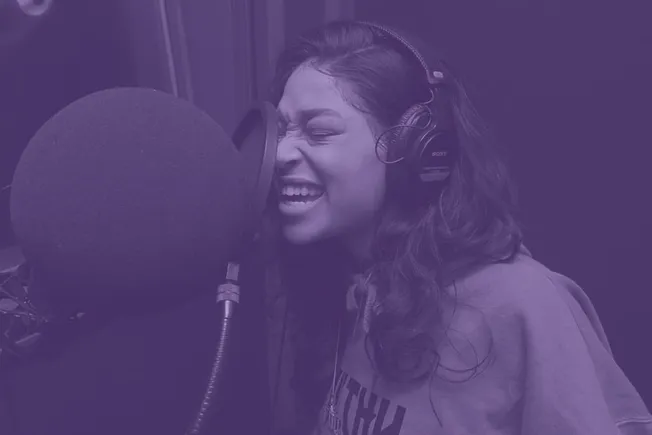 Female singer recording vocals in a professional studio with headphones, capturing high-quality audio for music production.