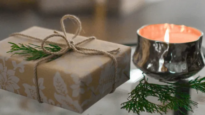 A beautifully wrapped holiday gift with a sprig of pine and a lit candle, creating a cozy festive atmosphere perfect for Chri
