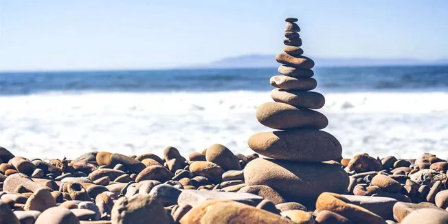 Balanced rocks stack on pebbled beach with ocean background, serenity, mindfulness, coastal landscape, zen stones, calm sea,