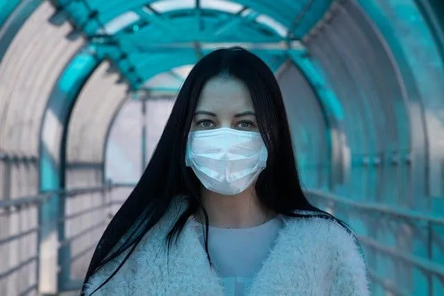 A woman with long dark hair wearing a protective face mask in a modern covered walkway, emphasizing health safety and urban e