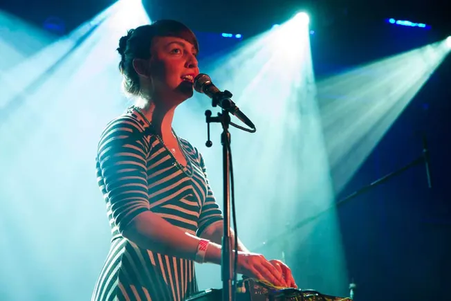 Female musician performing live on stage with microphone and electronic equipment at concert, stage lights, music, performanc
