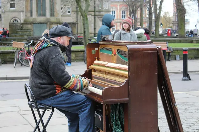 Vintage outdoor street piano player performing in a park during daytime in fall season.