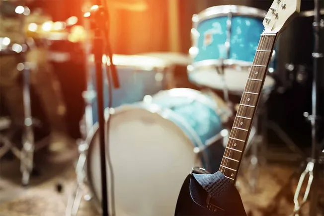 Electric guitar resting on a stage with a drum set in the background, perfect for music production, band practice, and live p