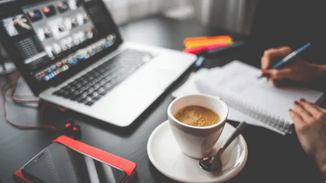 Laptop with video editing software, notebook, pen, smartphone, and coffee on a workspace – ideal for digital content creation