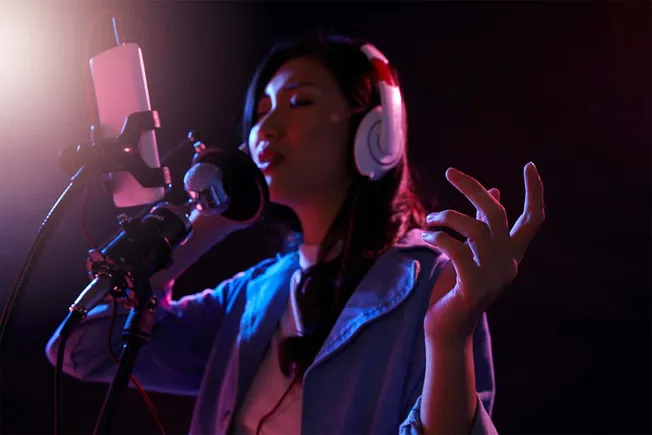 Professional female singer recording vocals in a dark studio with colorful lighting, wearing headphones and singing passionat
