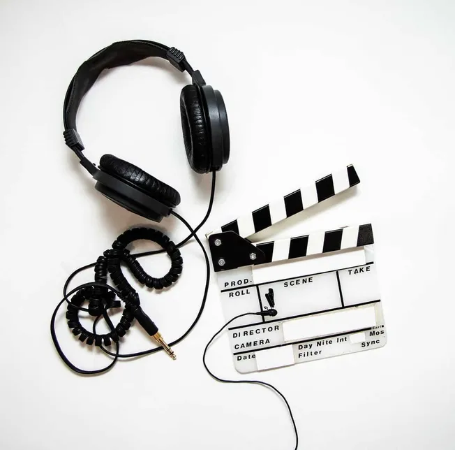 Headphones and film slate on white background for music production or film editing, highlighting audio-visual media creation