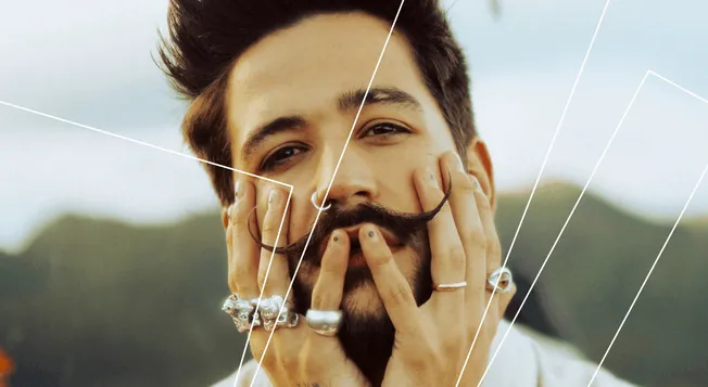 Vibrant portrait of a young man with styled hair and mustache, holding his face with hands adorned with silver rings, showcas