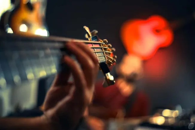 A person playing an electric guitar during a live performance with vibrant, colorful stage lighting in the background.