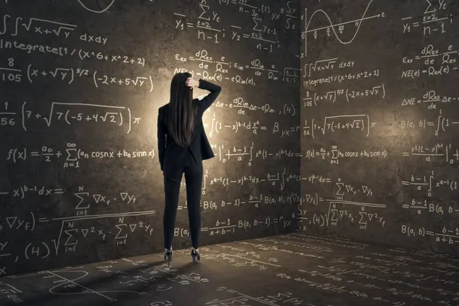 Complex mathematical equations written on a chalkboard with a woman in business attire analyzing data in a modern classroom.