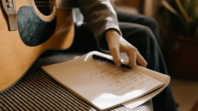 Guitarist taking notes with a pen on a notepad near an acoustic guitar, music songwriting, musicians brainstorming, creative