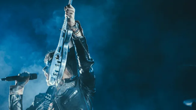 Rock musician performing with electric guitar on stage at concert under blue lights.