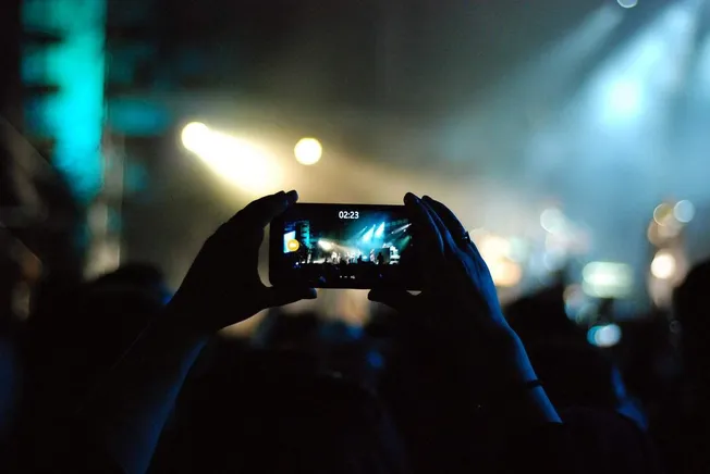Concert live music event captured with a smartphone in a dark setting with stage lighting and audience silhouette, vibrant bl