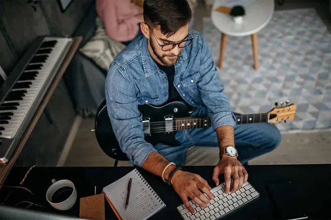 Young male musician composing at a music studio with keyboard, guitar, and keyboard.