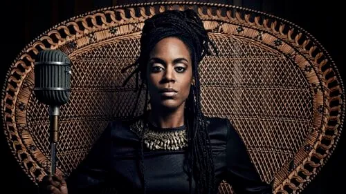 Microphone in front of a woman with dreadlocks sitting on an ornate chair, dark background, confident expression, music or po