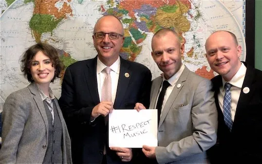 A diverse group of professionals standing together, holding a "#RespectMusic" sign, against a world map background, promoting