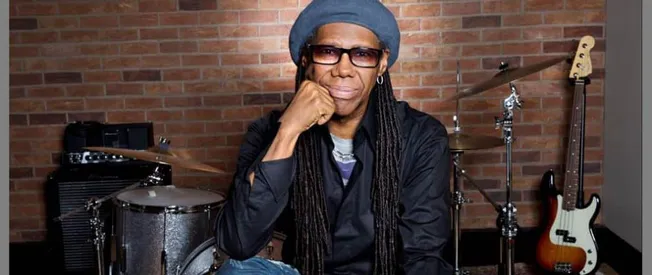 Creative musician with long dreadlocks and stylish accessories posing in a music studio with drums and a guitar for Hypebot S
