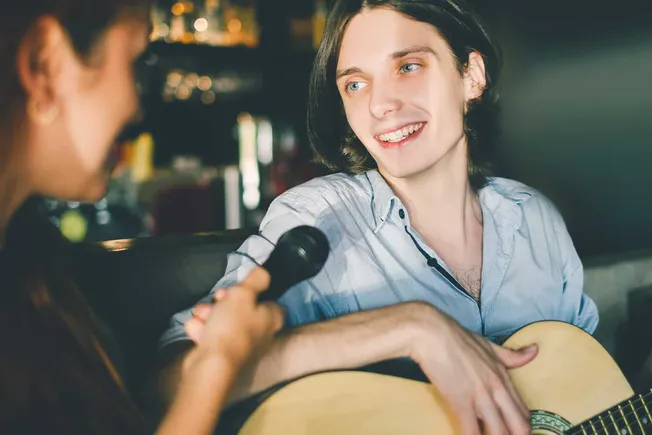 Young man playing guitar and singing with a woman holding a microphone in a cozy cafe setting, capturing musical performance