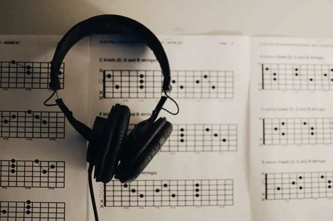 Headphones resting on guitar chord charts for music practice and guitar tutorials, representing music education and learning