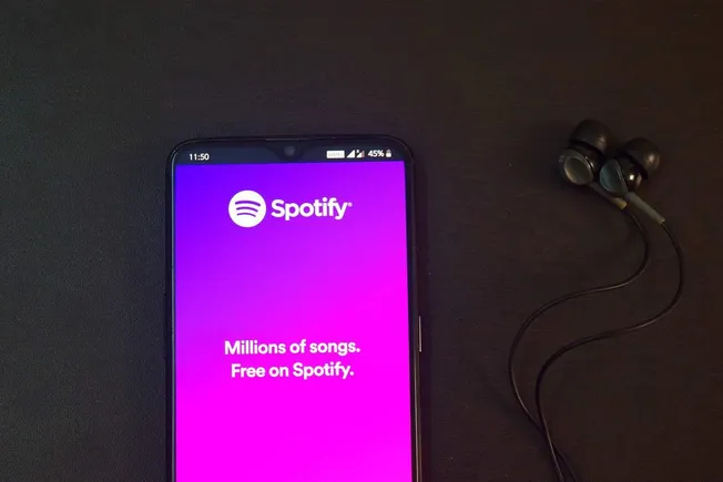 Spotify music app on smartphone with earphones, promoting music streaming service.