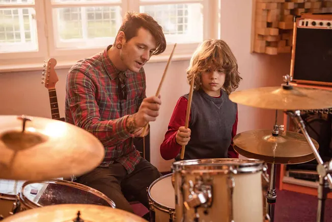 Teen boy and young man playing drums together in a music studio, practicing and learning music skills.