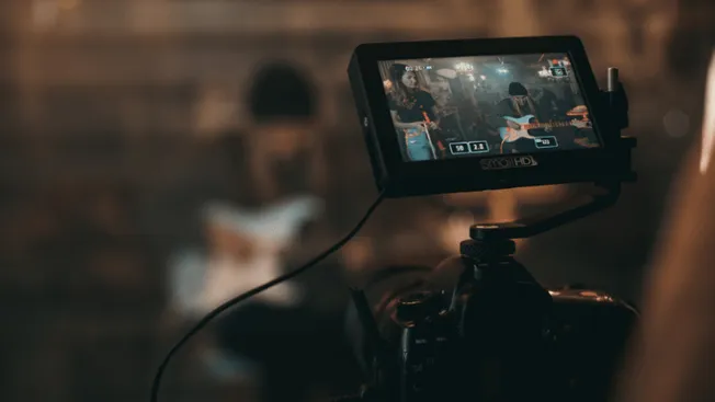 Professional music video recording setup with camera capturing live band performance in a studio. Advanced filming equipment