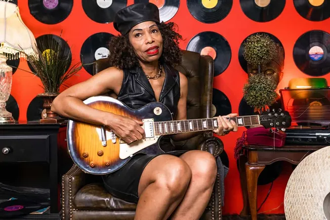 Vintage woman playing electric guitar in a retro music room with vinyl records, eclectic decor, and warm lighting, capturing