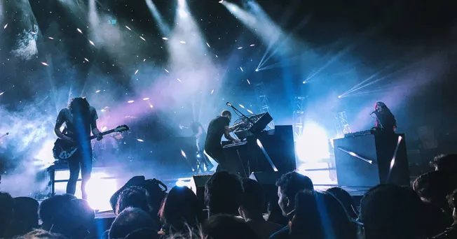 Handsome talented musicians performing live on stage with electric guitars, keyboards, and DJ equipment at a concert, illumin