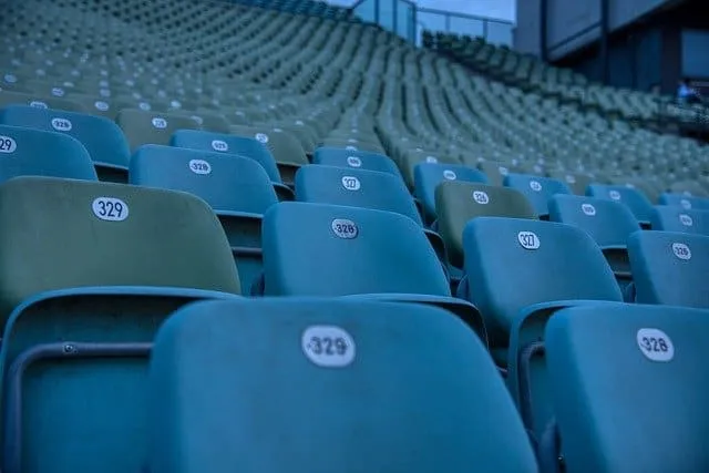 Empty stadium seats in a sports venue or concert hall, showcasing blue and green chairs arranged in rows for audience seating