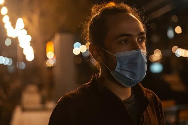 Young woman wearing a face mask outdoors at night, city lights blurred in the background, reflecting health precautions durin