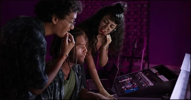 People collaborating in a music production studio using digital audio workstations, emphasizing music industry innovation and