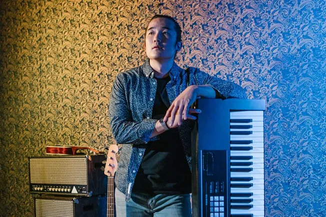 Vintage music studio with a young male musician leaning on a keyboard, surrounded by guitar amplifiers and a guitar, in a cre