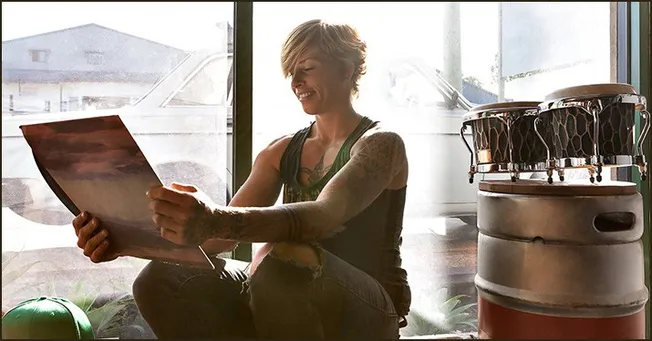 Young woman with tattoos reading a newspaper in a creative studio environment, with musical instruments around her, showcasin